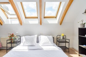 A bedroom with a skylight, a bed, a radiator, a small table with flowers, and a bookshelf. - Elegant Central CIty Apartment in Warsaw (Warszawa 2)