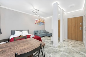 A modern living room with a dining table, a grey sofa, and a colorful abstract painting on the wall. - Stay with Free Parking (Łódź)