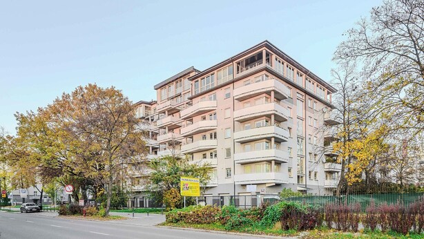 Ein mehrstöckiges Wohngebäude mit Balkonen, einem Parkplatz und Herbstlaub.