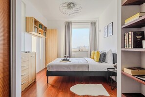 Ein Schlafzimmer mit Bett, Nachttisch, Bücherregal und Blick auf die Stadt.