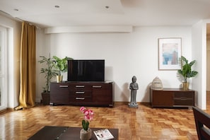 A living room with a flat-screen TV, wooden flooring, a dining table with chairs, and decorative plants. - Warsaw Home near Center (Warszawa 2)