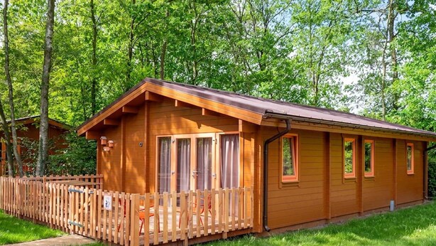 A wooden cabin with a fenced patio, surrounded by lush greenery.