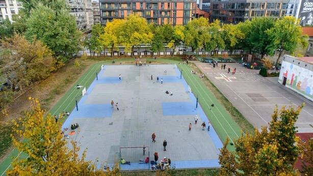 Un terrain de sport en plein air, entouré d’arbres et d’immeubles.