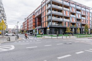 A modern multi-story building with a glass facade, pedestrian crossing, and a parking area.
