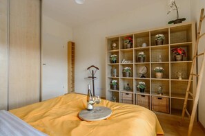 Une chambre à coucher comprenant un lit, une table de chevet avec une bouteille et des verres, une armoire en bois et une étagère avec des objets décoratifs.