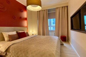 Ein Hotelzimmer mit einem großen Bett, einem Nachttisch, einer roten Akzentwand und einem Fenster mit Vorhängen.