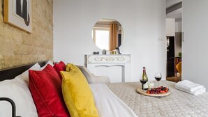 A hotel room with a bed, a bedside table with a mirror, a small kitchenette, and a breakfast tray with fruit and wine. - Warsaw Home with City Views (Warszawa)
