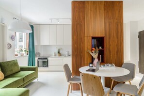 A modern living room with a green sofa, a dining table with four chairs, and a kitchen area with cabinets and a stove. - Convenient Base in Warsaw City Centre (Warszawa 2)
