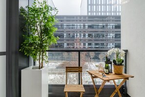A balcony with a wooden table, a chair, a potted plant, a bottle of wine, and a vase of flowers. - Convenient Base in Warsaw City Centre (Warszawa 2)