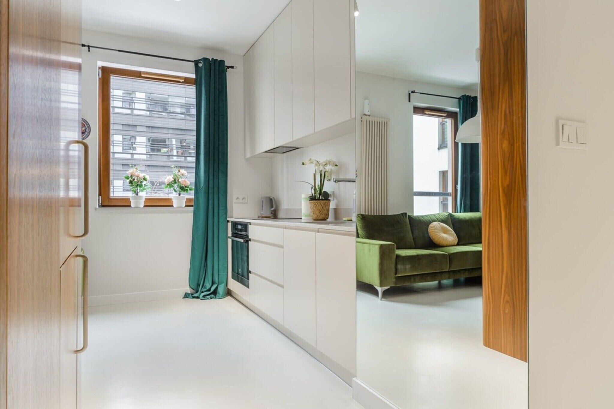 Een moderne keuken met witte kasten, een groene bank en een raam met gordijnen.
