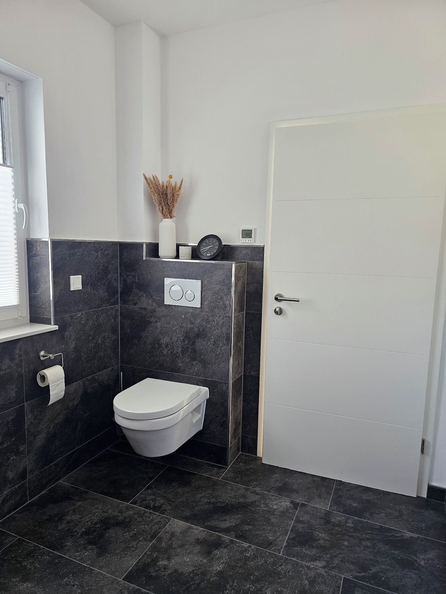Une salle de bain équipée de toilettes, d’un distributeur de serviettes et d’une horloge murale.