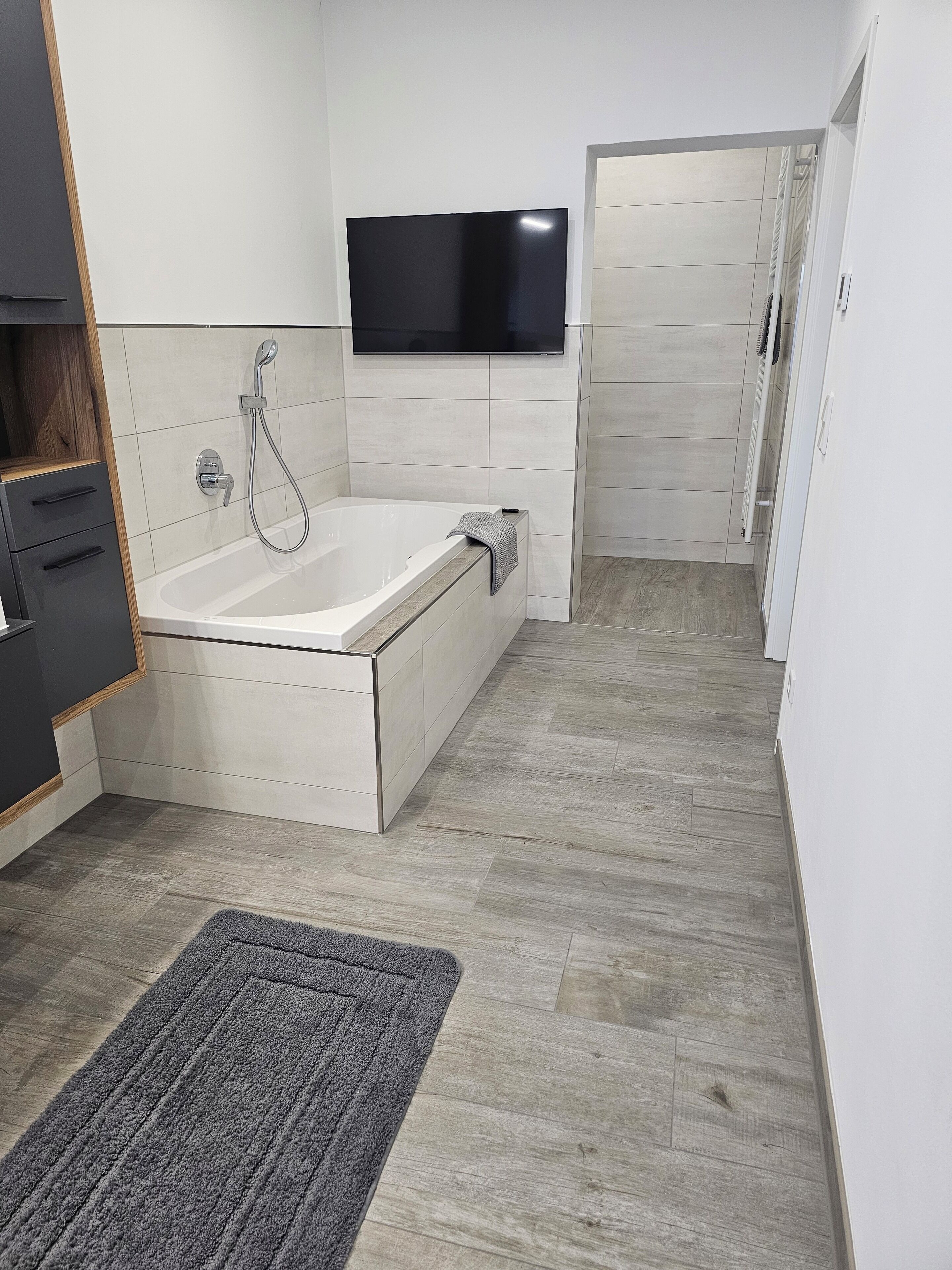 Une salle de bain moderne équipée d’une baignoire, d’une douche et d’un téléviseur à écran plat fixé au mur.