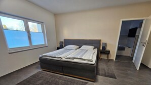 Ein Schlafzimmer mit einem Bett, Nachttischen, einem Fenster und einer Tür zu einem Badezimmer.