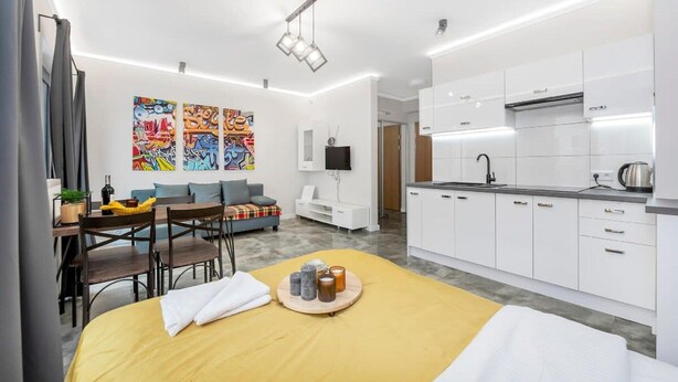 A modern kitchen with white cabinets, a black faucet, and a kettle on the counter. - Home near Piotrkowska Street (Łódź)