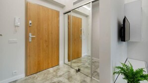 A hallway with wooden doors, a glass partition, a mounted television, and a potted plant. - Home near Piotrkowska Street (Łódź)