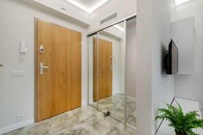 A hallway with wooden doors, a glass partition, a mounted television, and a potted plant. - Home near Piotrkowska Street (Łódź)