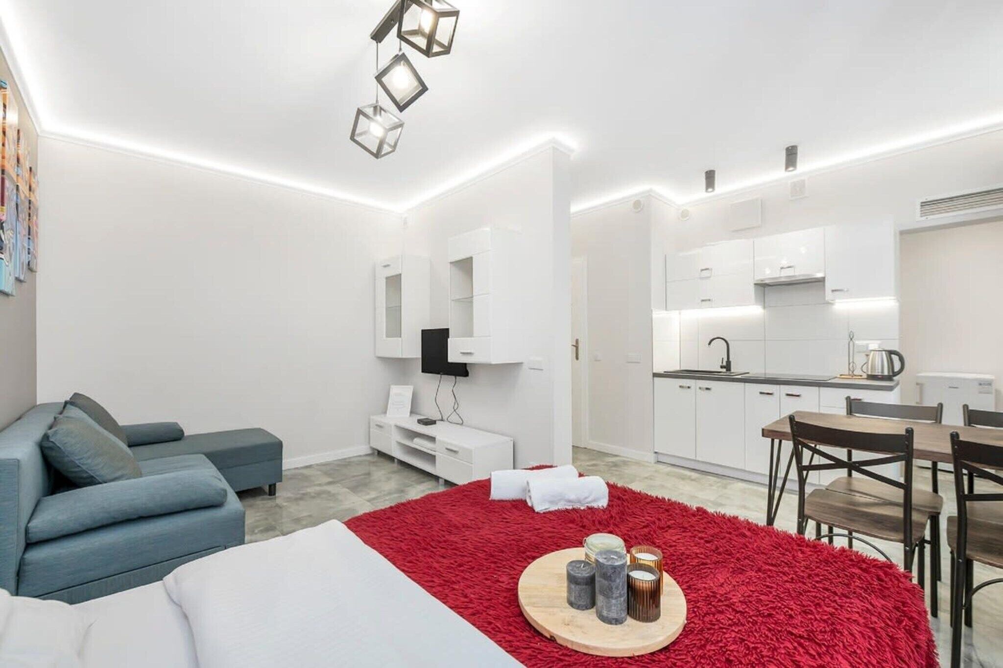 Une chambre d’hôtel moderne avec un canapé, un tapis rouge, une table à manger et un coin cuisine.