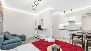 A modern hotel room with a sofa, a red rug, a dining table, and a kitchen area. - Quiet Stay near Manufaktura (Łódź)