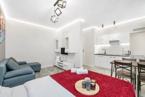 A modern hotel room with a sofa, a red rug, a dining table, and a kitchen area. - Quiet Stay near Manufaktura (Łódź)