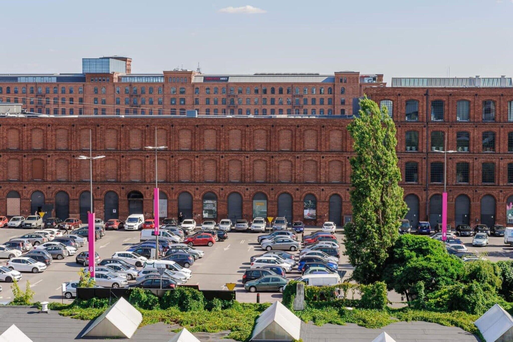 A parking lot with multiple cars and a large brick building in the background.