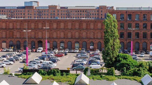 A parking lot with multiple cars and a large brick building in the background. - Quiet Stay near Manufaktura (Łódź)