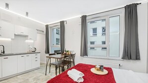 A hotel room with a bed, a dining table with chairs, a kitchen area, and a window with curtains. - Quiet Stay near Manufaktura (Łódź)
