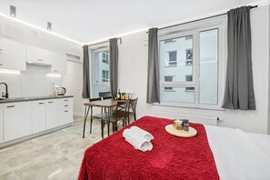 A hotel room with a bed, a dining table with chairs, a kitchen area, and a window with curtains. - Quiet Stay near Manufaktura (Łódź)