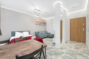 A modern living room with a dining table, a grey sofa, and a colorful abstract painting on the wall. - Quiet Stay near Manufaktura (Łódź)