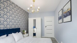 A bedroom with a bed, a nightstand, a chandelier, a wardrobe, and two framed pictures on the wall. - House by Plage de Melon with Garden Retreat (Łódź)