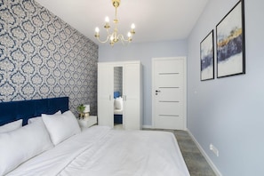 A bedroom with a bed, a nightstand, a chandelier, a wardrobe, and two framed pictures on the wall. - House by Plage de Melon with Garden Retreat (Łódź)