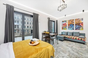 A modern hotel room with a bed, a dining table with chairs, a sofa, and a large window with curtains. - Central Haven near Station (Łódź)
