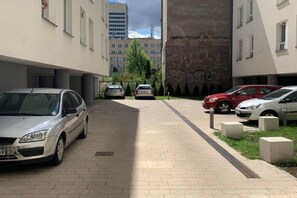 A parking area with cars parked along a paved path, surrounded by buildings with windows and a brick wall. - Central Haven near Station (Łódź)
