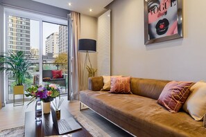 A modern living room with a sofa, a coffee table with a laptop, a floor lamp, and a large window with a view of buildings. - Flat on Grzybowska Street (Warszawa)