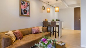 A modern living room with a brown sofa, a dining area with two chairs, pendant lights, and a kitchen area with a refrigerator. - Flat on Grzybowska Street (Warszawa)
