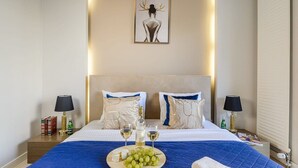 A hotel room with a large bed, two bedside tables, a nightstand, a framed artwork on the wall, and a blue blanket on the bed. - Flat on Grzybowska Street (Warszawa)