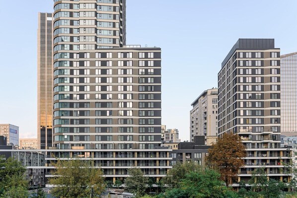 Ein modernes Hochhaus mit einer geschwungenen Fassade, mehreren Balkonen und einer Kombination aus Glas- und Vollwandfenstern.