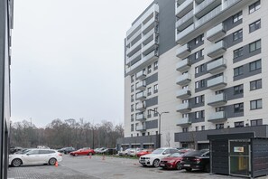 En flervåningsbyggnad med bostäder, balkonger, en parkeringsplats med bilar och en grind vid ingången.