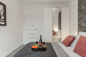 Ein Schlafzimmer mit einem Bett, einem Nachttisch mit einer Weinflasche und Gläsern sowie einer Obstplatte.