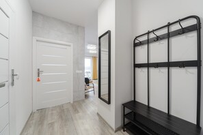 A hallway with a white door, a mirror, and a black metal rack with hooks. - City Haven near Atlas Arena (Łódź)