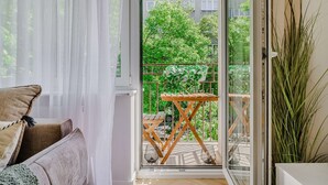 Ein Balkon mit Holztisch und Stühlen, Blick auf Grünflächen und ein Gebäude im Hintergrund.