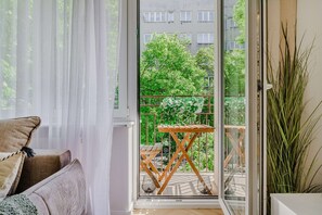 A balcony with a wooden table and chairs, a view of greenery, and a building in the background. - Charming Apartment near the beach (Warszawa 2)
