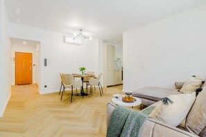A modern living room with a sofa, a coffee table, and a dining area with chairs and a table. - Premium Warsaw City Apartment with Balcony (Warszawa 2)