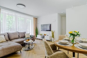 A modern living room with a sofa, coffee table, and dining table set for a meal. - Charming Apartment near the beach (Warszawa 2)