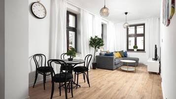 Un salon moderne avec un coin repas, comprenant une table ronde, des chaises noires, un canapé gris et une petite table d’appoint.