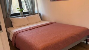 A bed with a pink quilt, a window with curtains, and a potted plant on the windowsill. - Flat near Piotrkowska Street (Łódź)