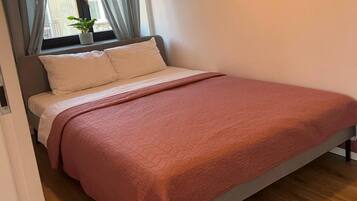 Un lit recouvert d’une couette rose, une fenêtre avec des rideaux et une plante en pot posée sur le rebord de la fenêtre.