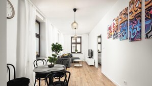 A modern living room with a dining area, wooden flooring, a potted plant, a grey sofa, and a TV. - Flat near Piotrkowska Street (Łódź)