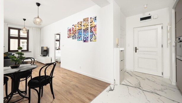 A modern kitchen with white cabinets, a marble countertop, and a dining area with a table and chairs. - Flat near Piotrkowska Street (Łódź)