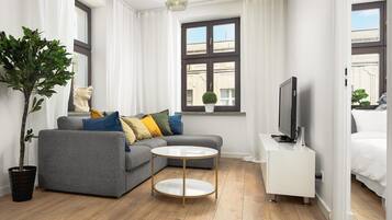 Un salon moderne avec un canapé gris, une table basse ronde, un téléviseur et une plante en pot.