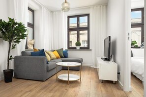 Ein modernes Wohnzimmer mit einem grauen Sofa, einem runden Couchtisch, einem Fernseher und einer Topfpflanze.